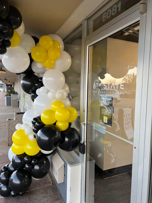 Balloon garland adorning front of business door. Garland is yellow, black, and white in color.
